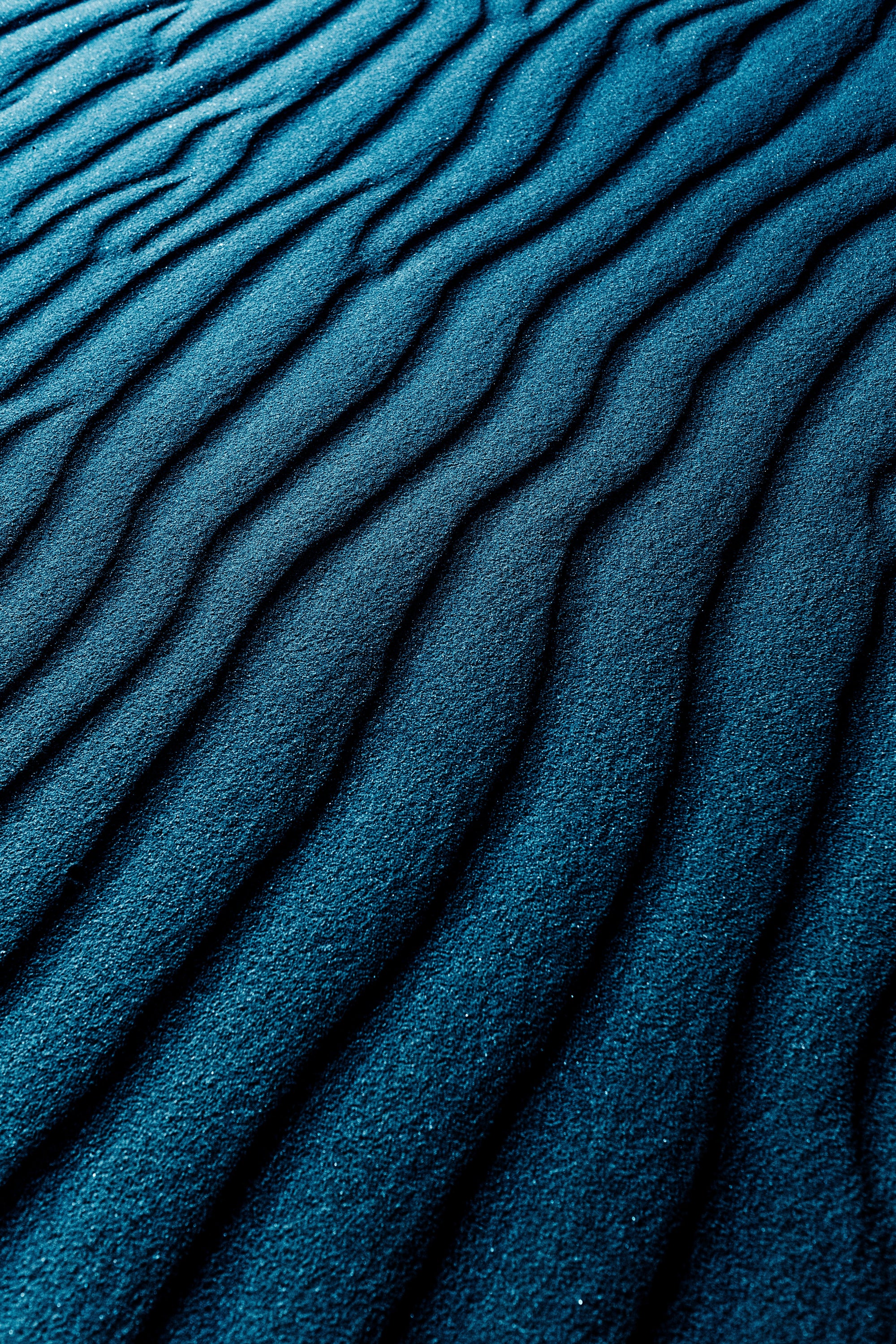 Ein Bild zeigt blauen wellig geformten dunklen Sand